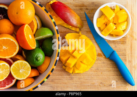 Slicing and preparing fresh healthy tropical fruit with a ripe juicy mango and assorted citrus fruit including oranges, clementine, grapefruit, lime a Stock Photo