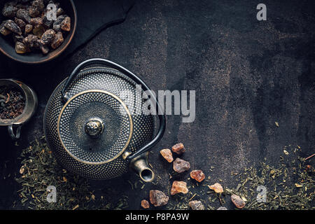 Teapot, rock of sugar and assortment of dry tea on black table. Top view with copy space Stock Photo