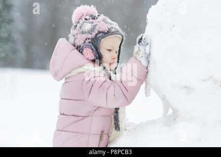 Funny little girl having fun in beautiful winter park during snowfall Stock Photo