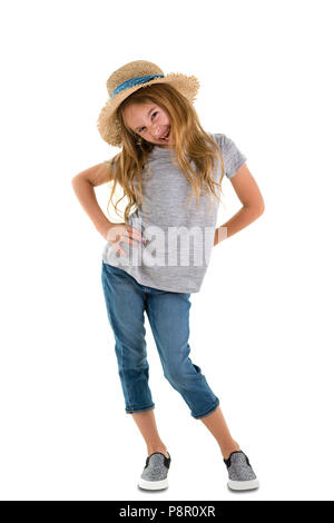 Mischievous playful 6 year old little girl with long tousled blond hair and a cute grin wearing trendy jeans and a straw hat standing with hands on hi Stock Photo