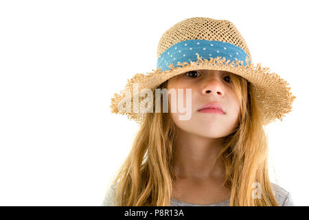 Serious little girl with long blond hair peering out from under a trendy straw hat with blue ribbon at the camera isolated on white Stock Photo