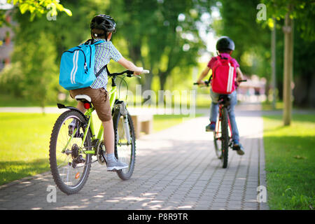 Children with rucksacks riding on bikes in the park near school Stock Photo