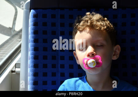 Child sleeps with nipple in mouth on a train ride and dreams Stock Photo
