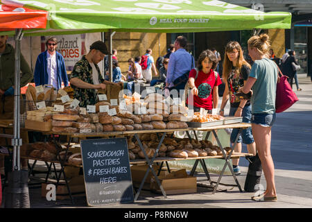 A small food market outside Kings Cross with baked breads and other produce for sale with customers browsing goods, London, UK Stock Photo