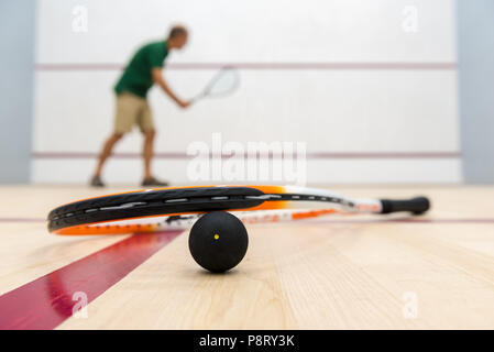 Squash racket lying on ball with player in the background Stock Photo