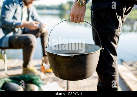 Two fishermen preparing some food during the picnic on the wooden pier near the lake in the morning Stock Photo