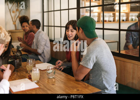 Smiling friends sitting and talking together at a bistro table Stock Photo