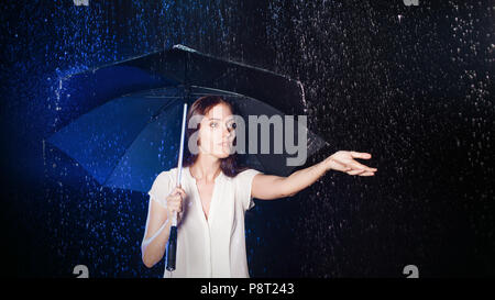 Young woman under umbrella. Protection from rain. Brunette girl holding an umbrella. Portrait in Studio on black background. Concept of optimism Stock Photo
