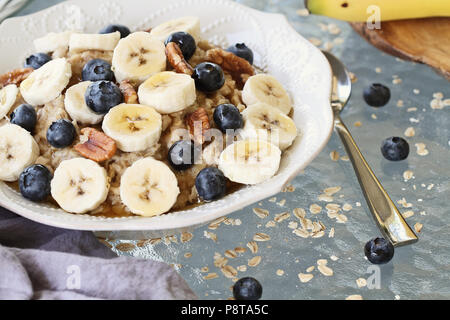 Hot breakfast of healthy oatmeal with pecans, bananas, blueberries and honey over a rustic background. Image shot from overhead. Stock Photo