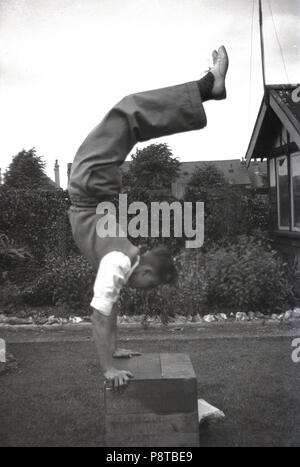 1950s, historical, young man, wearing clothes, doing a handstand on a wooden crate outside in a back garden, England, UK. Stock Photo