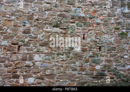 Texture of brown with green mold of stone. Old, medieval wall of a building in Italy. Background from natural, ancient cobblestones Stock Photo