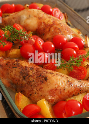 Tasty roasted chicken legs with potatoes and fresh herbs in a glass pan Stock Photo