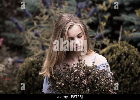 teenage beautiful girl with blonde hair standing next to a tree with flowers Stock Photo