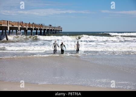 Three surfers heading out into the water at Jacksonville Beach, Florida Stock Photo