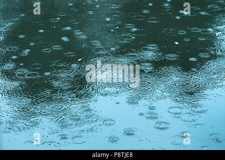 rain drops rippling in a puddle blue tone. Stock Photo