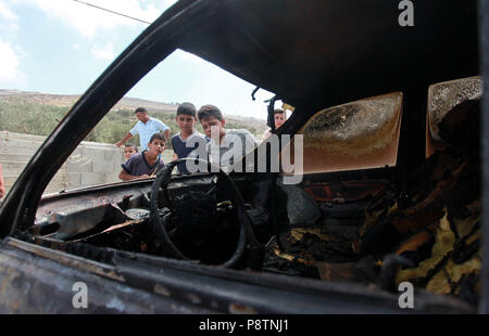 Nablus, Urif village near the West Bank city of Nablus. 13th July, 2018. Palestinian boys inspect a burned car after Jewish settlers set them on fire, in Urif village near the West Bank city of Nablus, on July 13, 2018. Earlier on Tuesday, Palestinian sources said that settlers from settlement of Yitzhar raided the village of Urif near Nablus and burned two Palestinian cars. Credit: Nidal Eshtayeh/Xinhua/Alamy Live News Stock Photo