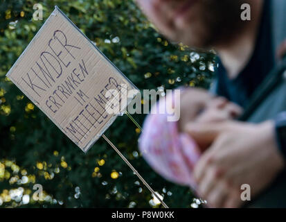 Germany, Hamburg. 13th July, 2018. Demonstrators in the district of St. Pauli carry signs reading 'Children are drowning in the Mediterranean Sea'. The protest for sea rescue of refugees in the Mediterranean is happening under the slogan 'Seebrücke · Schafft sichere Häfen!'. Credit: Axel Heimken/dpa/Alamy Live News Stock Photo