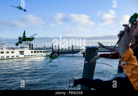 Germany, Hamburg. 13th July, 2018. Demonstrators cast flowers into the river Elbe in remembrance of the drowned refugees in the Mediterranean. The protest for sea rescue of refugees in the Mediterranean is happening under the slogan 'Seebrücke · Schafft sichere Häfen!' (lit. 'Sea bridge - create safe harbours!'). Credit: Axel Heimken/dpa/Alamy Live News Stock Photo