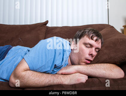 Guy passed out on couch with arms wrapped around a pillow Stock Photo