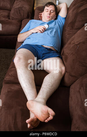 Wide angle view of man laying on couch holding remote Stock Photo