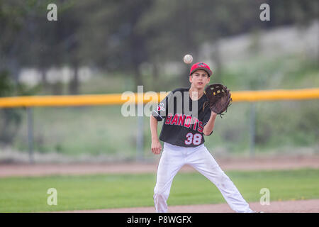 Ball just before hitting glove of infielder, boys afternoon junior baseball game. Cranbrook, BC. Stock Photo