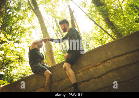 Fit man assisting his teammate to climb a wooden wall Stock Photo