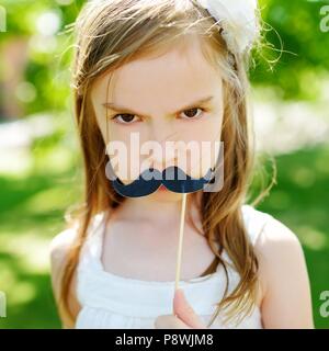 Adorable little girl playing with paper moustache on a stick on warm summer day Stock Photo