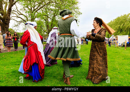 Medieval dancing outdoors. Living history group of people dressed in traditional costume dancing on the grass with large tree in background. Stock Photo