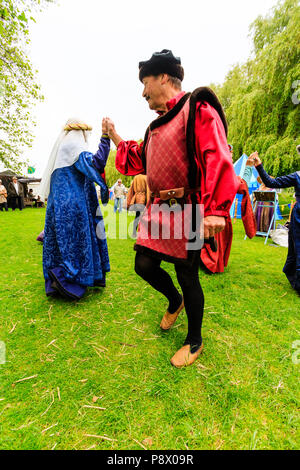 Medieval dancing outdoors. Living history group of people dressed in traditional costume dancing on the grass with trees in background. Stock Photo