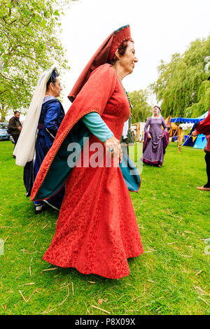 Medieval dancing outdoors. Living history group of people dressed in traditional costume dancing on the grass with trees in background. Stock Photo