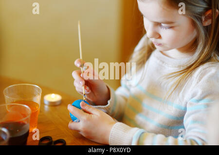 Adorable little girl coloring an Easter egg using wax and dyes Stock Photo