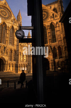 York Minster South transept from Minster Gates. Silhouette of man carrying briefcase as he walks beneath a shop clock at 9.23am Stock Photo