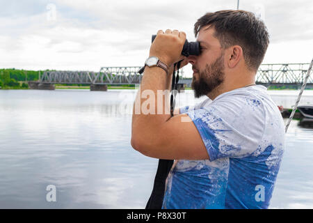 Captain looks through a binoculars - marine concept. Young man with beard on a yacht Stock Photo