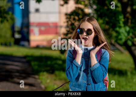 Girl schoolgirl teenager. Summer nature. In jeans clothes, sunglasses. The concept of surprise, surprises, gift, surprise. Emotions of joy of happiness and delight, Scream and exclamations. Stock Photo