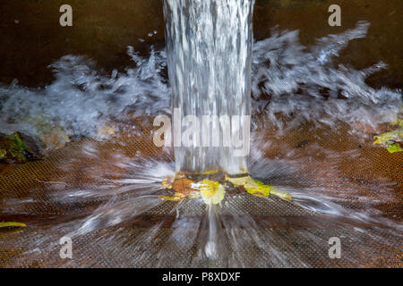 Crystal-clear water flowing from a v-notch weir splashing as it falls on leaves Stock Photo