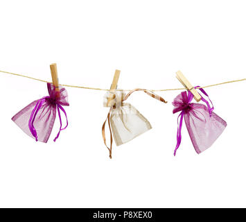 Three colored little gift bags hanging on a rope with clothespins isolated on white background. Stock Photo