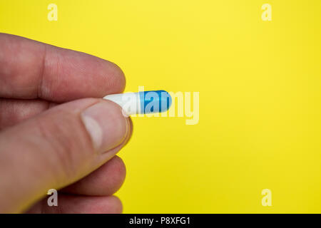 Hand holding drugs pills capsule on bright yellow background Stock Photo