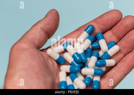 Hand holding drugs pills capsules on blue color background Stock Photo