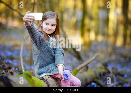 Adorable little girl taking a photo of herself in the woods on beautiful sunny spring day Stock Photo