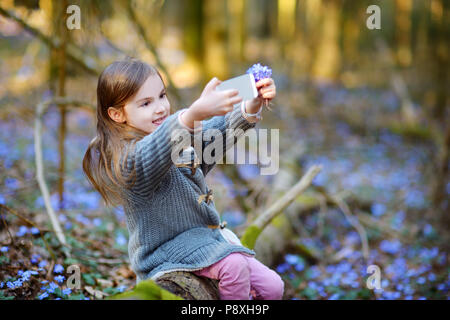 Adorable little girl taking a photo of herself in the woods on beautiful sunny spring day Stock Photo