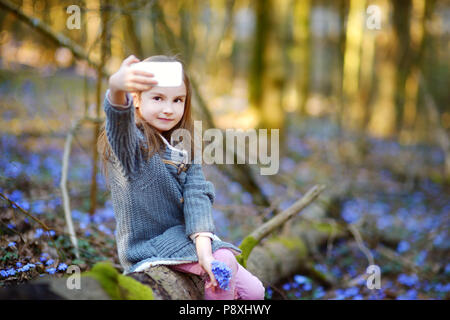 Adorable little girl taking a photo of herself in the woods on beautiful sunny spring day Stock Photo