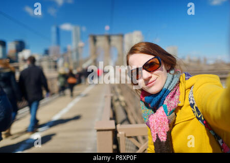 Beautiful young woman taking a selfie with her smartphone on Brooklyn Bridge, New York, at sunny spring day