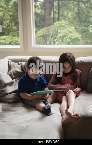 Siblings using digital tablet in living room Stock Photo