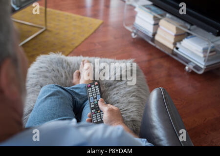 Man changing channels while watching television in living room Stock Photo
