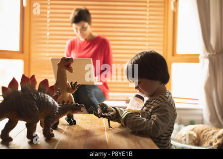 Boy playing toys while mother using laptop Stock Photo