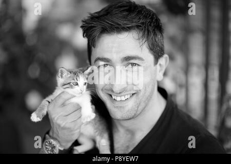 Young man holding a kitten in his hands and smiling black and white photo Stock Photo