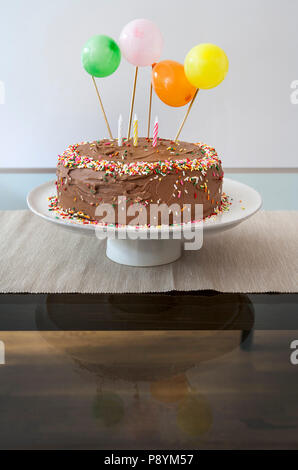 Birthday Cake with Chocolate Icing Decorated with Balloons, Sprinkles and Candles Stock Photo