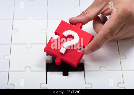 Close-up of a person's hand placing red question mark piece into jigsaw puzzle Stock Photo