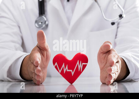 Doctor's hand protecting red heart rate on desk Stock Photo