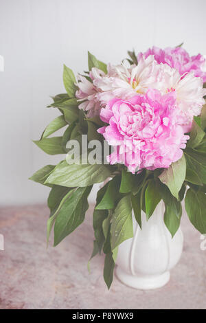 Delicate pink and white peonies in a white beautiful vase on a marble table Stock Photo